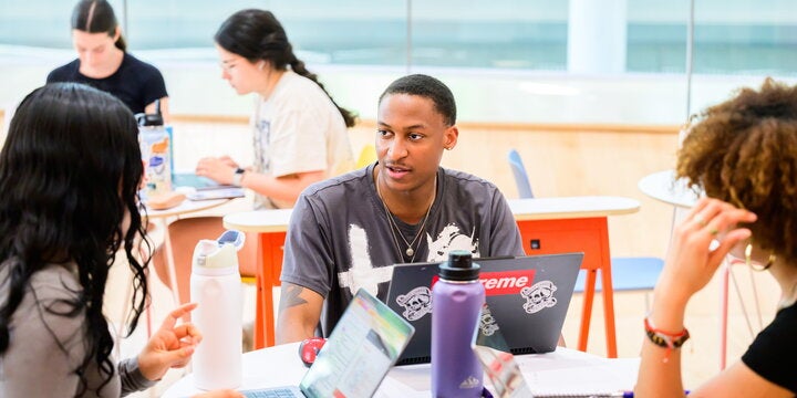 Students studying at table with laptops.